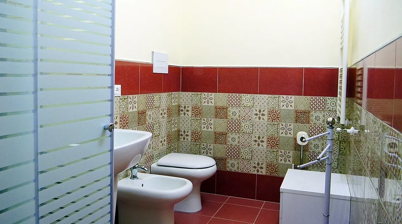 A bathroom with a toilet, bidet, and sink. The walls are tiled with a patterned design.