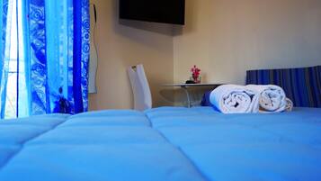 A hotel room with a bed, a small table with a vase of flowers, and a TV mounted on the wall.