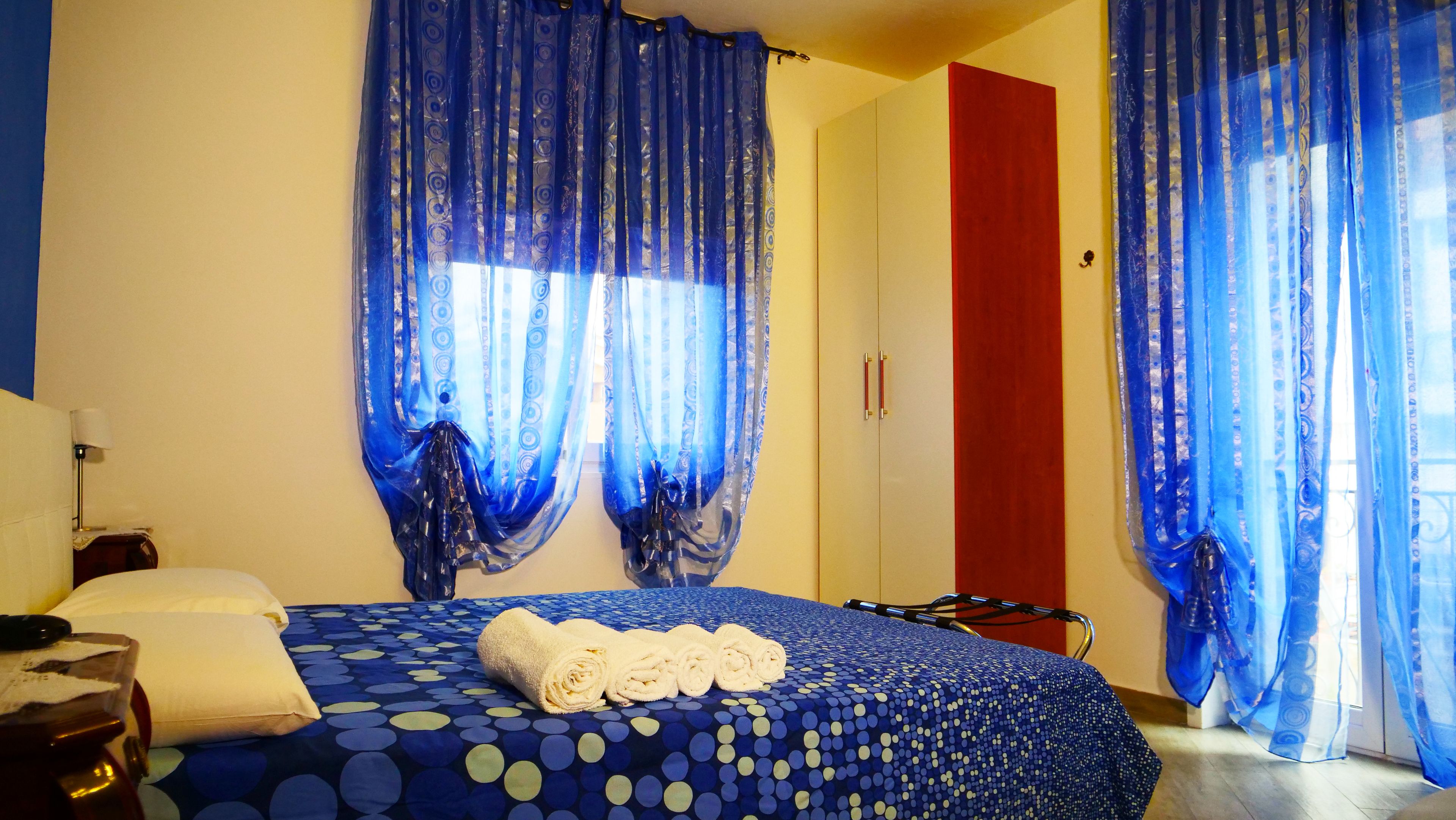 A hotel room with a bed, a red wardrobe, and blue curtains.