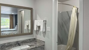 Un bany amb un lavabo de marbre, un mirall gran, una banyera i una cortina de bany.
