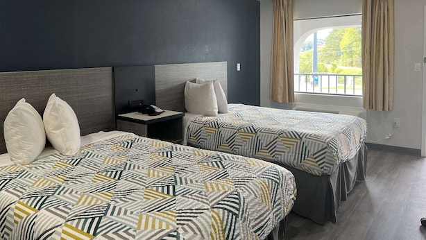 Una habitació d'hotel amb dos llits, una tauleta de nit, un telèfon i una finestra amb cortines.