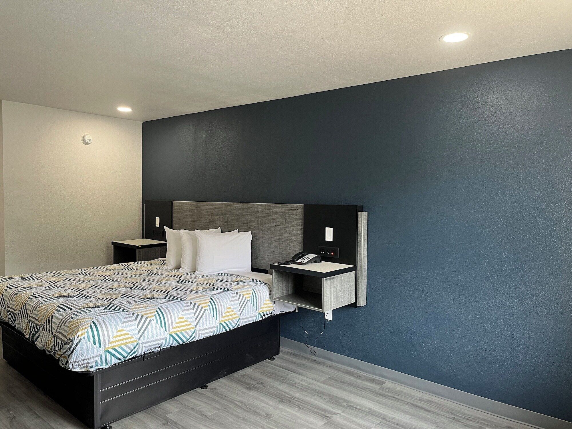 A modern hotel room with a large bed, a bedside table, a nightstand, a built-in desk, and a telephone.