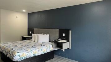 A modern hotel room with a large bed, a bedside table, a nightstand, a built-in desk, and a telephone.