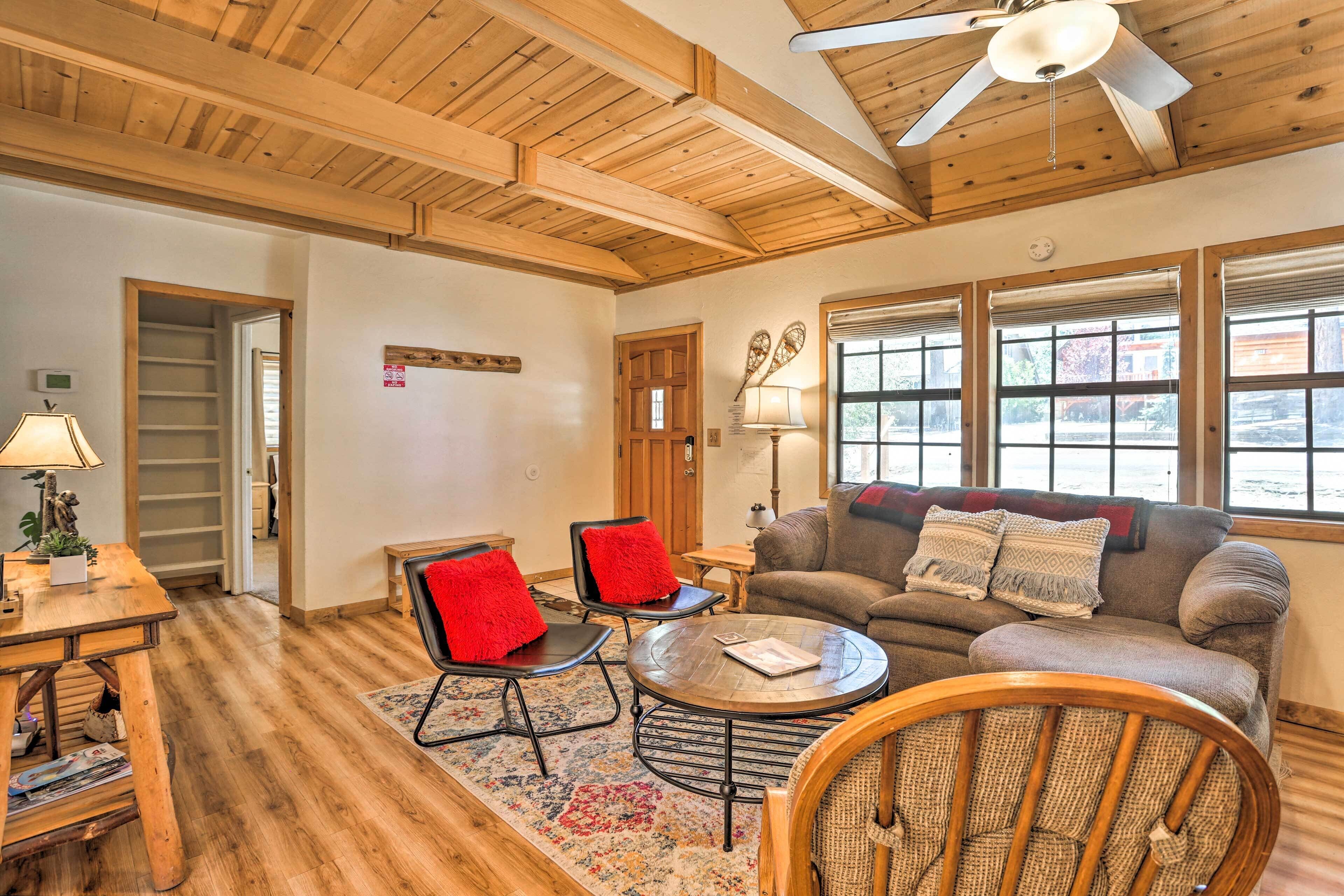 A cozy living room with wooden floors, a ceiling fan, a sofa with red cushions, and a coffee table.