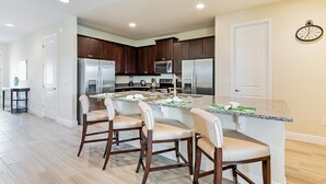 Une cuisine moderne avec des meubles en bois foncé, des appareils électroménagers en acier inoxydable et un îlot central doté de tabourets de bar.