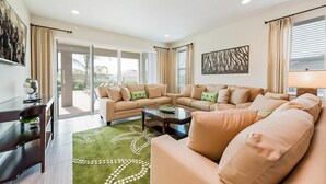 Un salon spacieux comprenant un grand canapé, une table basse et un tapis vert orné d’un motif blanc.