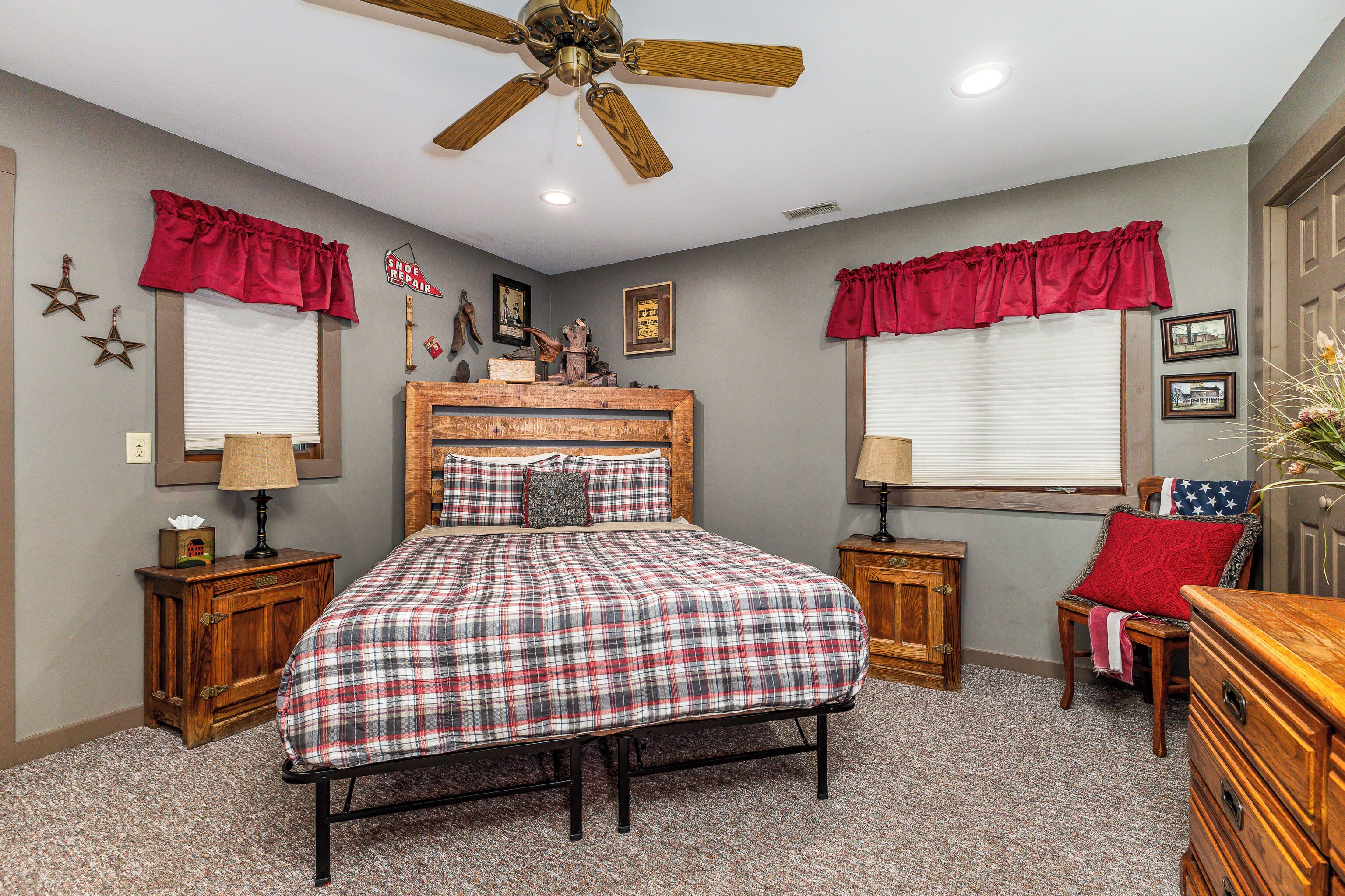 A bedroom with a bed, two nightstands, a dresser, a ceiling fan, and a window with a red valance.