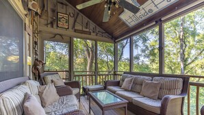 Une véranda couverte, meublée de meubles en osier, avec une table à plateau de verre et une enseigne indiquant « Hillside House ».