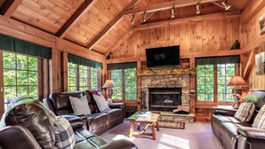 Un intérieur chaleureux de chalet en bois, avec une cheminée en pierre, des canapés en cuir et de grandes fenêtres.