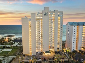 A high-rise hotel with multiple floors, a prominent logo on the facade, and a view of the ocean.