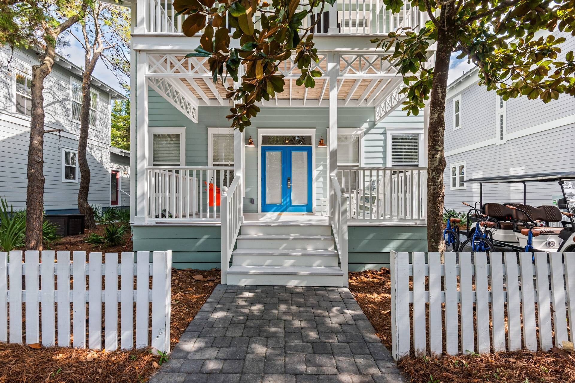 Uma casa de dois andares com porta azul, guarda-corpos brancos e varanda coberta.