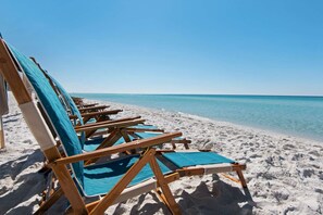 A row of wooden beach chairs with blue cushions on a sandy beach, facing a calm sea under a clear sky. - 4 Free bikes & Free 6 Seater Golf Cart/Short Walk to Beach/2 Community Pools-one heated/Summers Edge (Seagrove Beach)