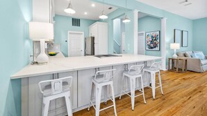 Una cocina moderna con una isla grande, taburetes blancos tipo bar e iluminación colgante.