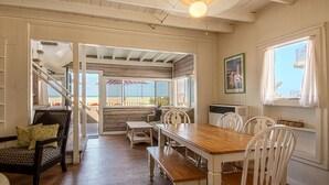 A dining area with a wooden table and white chairs, a staircase leading to an outdoor balcony, and a framed picture on the wall.
