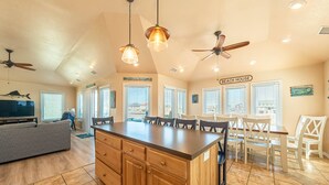 A spacious kitchen with a central island, wooden cabinets, and a dining area with white chairs. - Shorenuff - Nags Head MP 11, Ocean View, Beach 200 Yds, Pool, Hot Tub, Pool Table, YR Flex Stays (Nags Head)