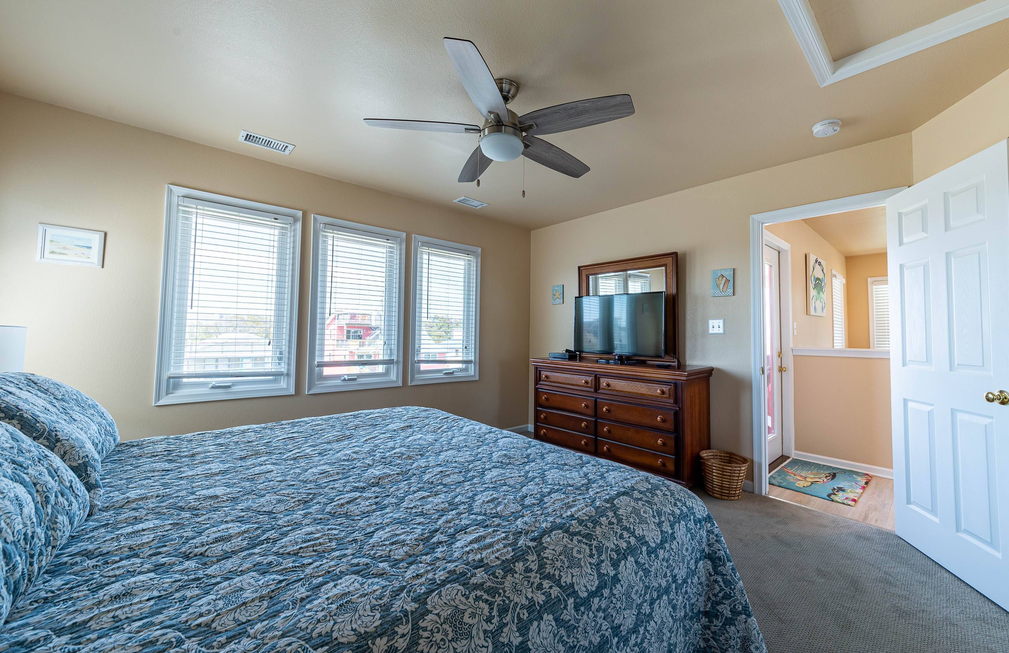 Une chambre à coucher comprenant un lit, une commode, un ventilateur de plafond et un téléviseur.