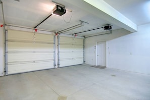 Eine Garage mit zwei geschlossenen Garagentoren, einem an der Decke befestigten Projektor und einer Tür mit einer kleinen Stufe, die zum Garageneingang führt.