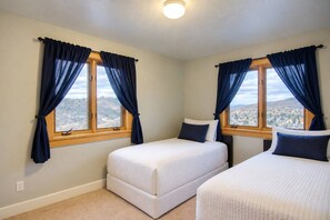 A room with two beds, a window with curtains, and a view of a cityscape.