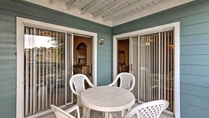 Un patio cubierto con una mesa redonda y cuatro sillas, una puerta corrediza de vidrio y una pequeña área de cocina visible a través de la puerta.