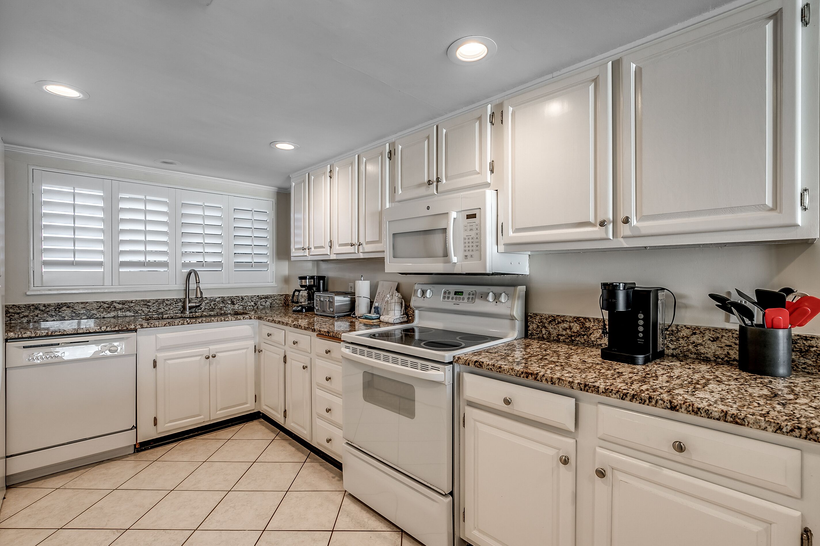 A modern kitchen with white cabinets, granite countertops, a built-in microwave, and a stainless steel oven.