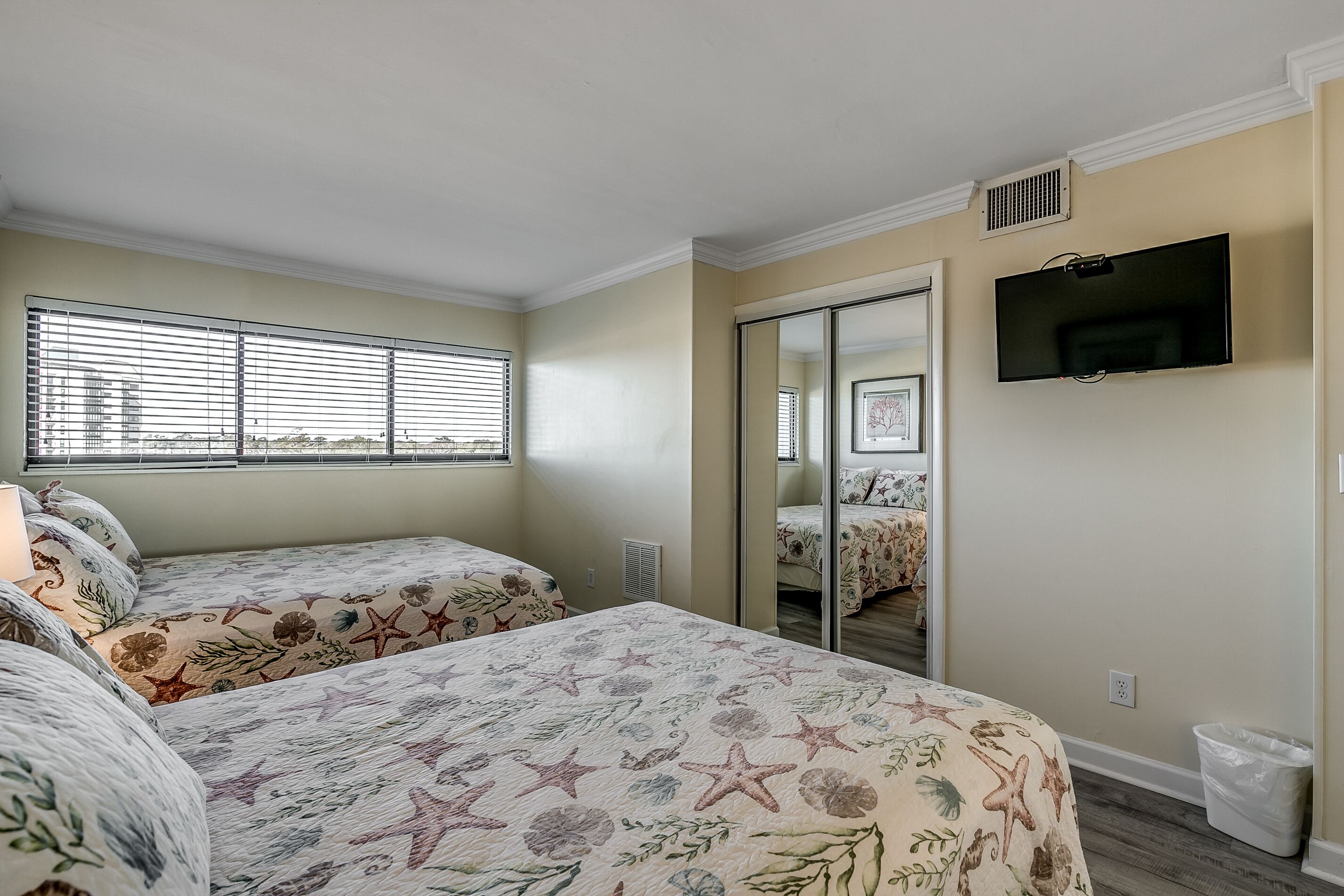 A bedroom with two beds, a TV, and a window with blinds.