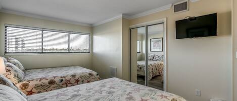 A bedroom with two beds, a TV, and a window with blinds.