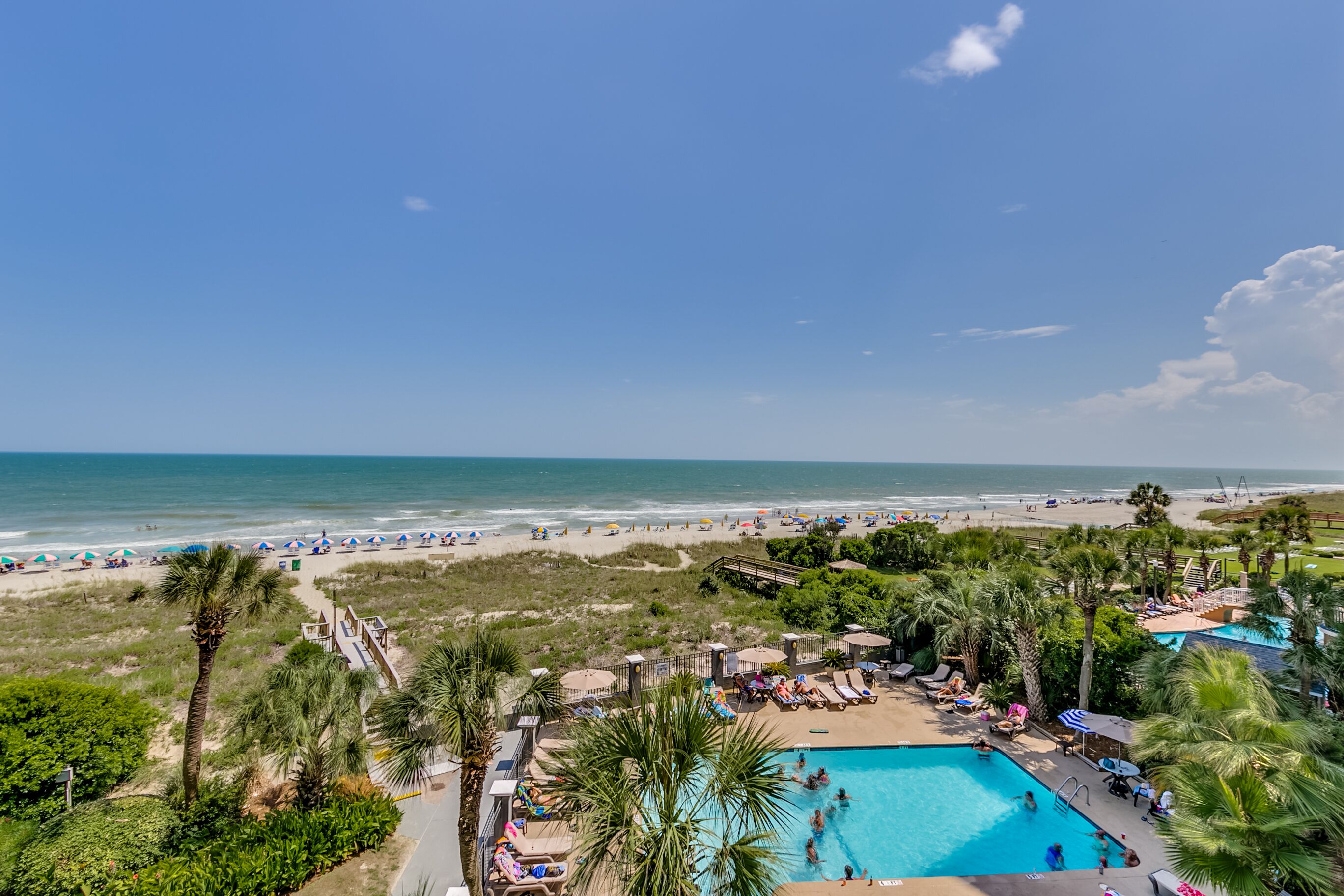 Un complexe hôtelier doté d’une piscine, d’une plage et de palmiers.