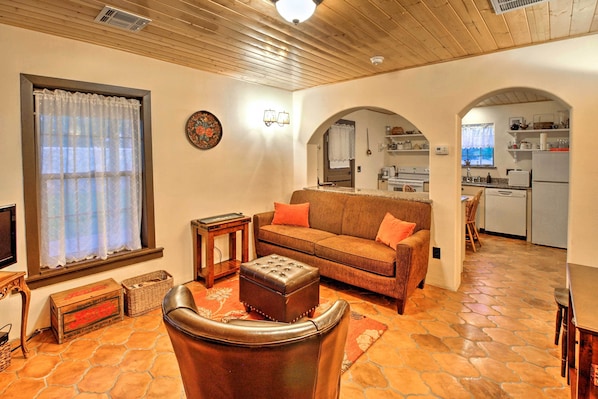 Un salón acogedor con un sillón de cuero, un sofá marrón y una mesa de centro de madera. Se ve una cocina a través de un arco.