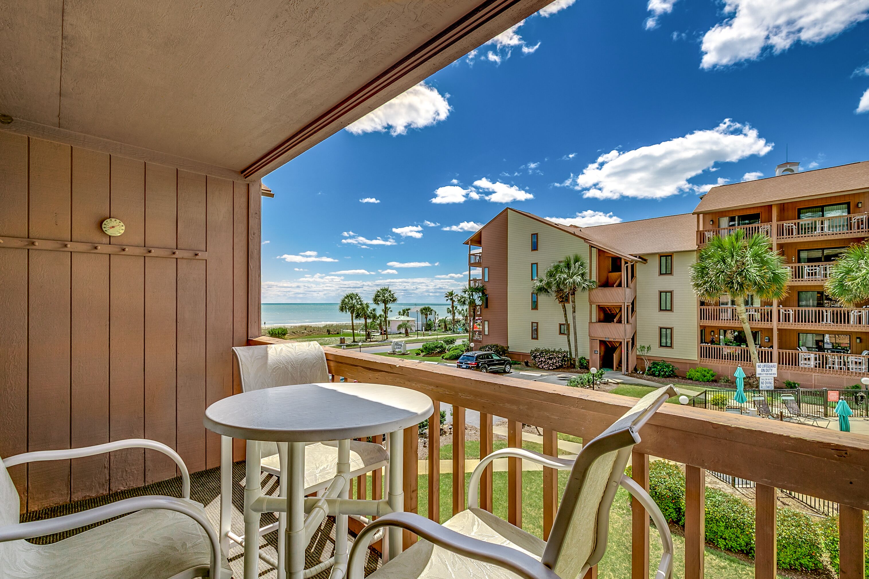 Un balcone con tavolo e sedie, con vista su una spiaggia e edifici con palme.