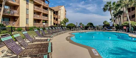A poolside area with sun loungers and a clear blue pool, surrounded by a multi-story building with balconies.