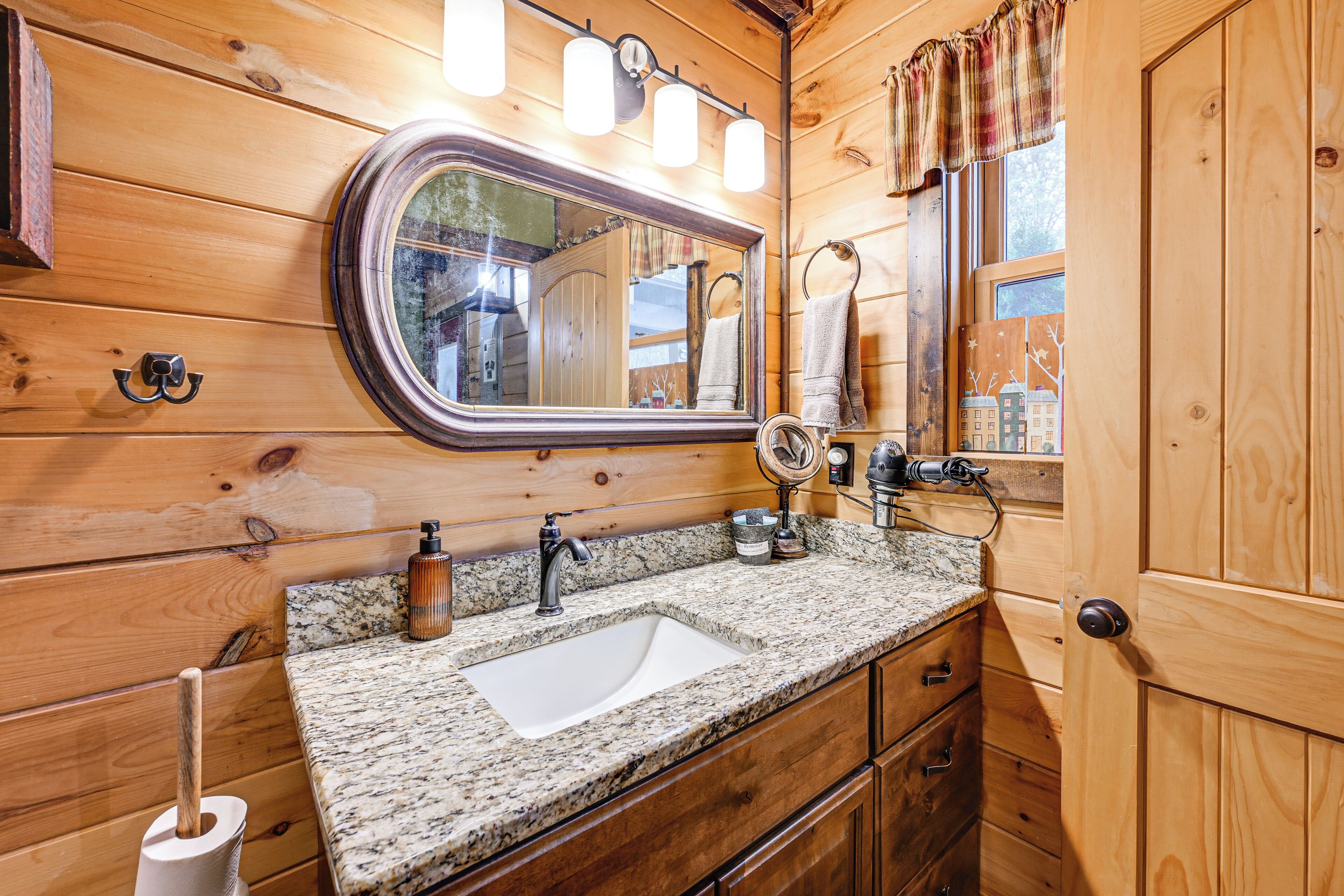 Une salle de bain rustique, avec une cabine en bois, un lavabo sur un plan de travail en granit, un grand miroir et des murs en bois.