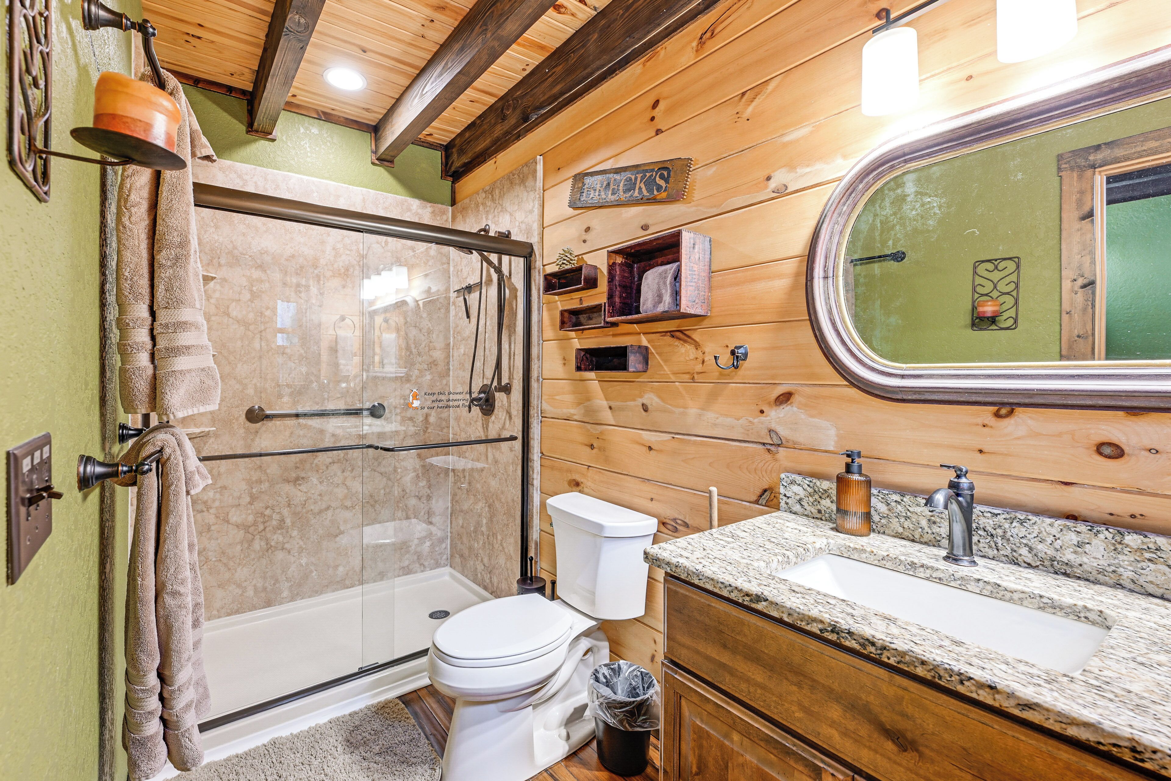 Une salle de bain avec une douche à parois de verre, des toilettes, un lavabo avec un plan de travail en granit et un lambris en bois.