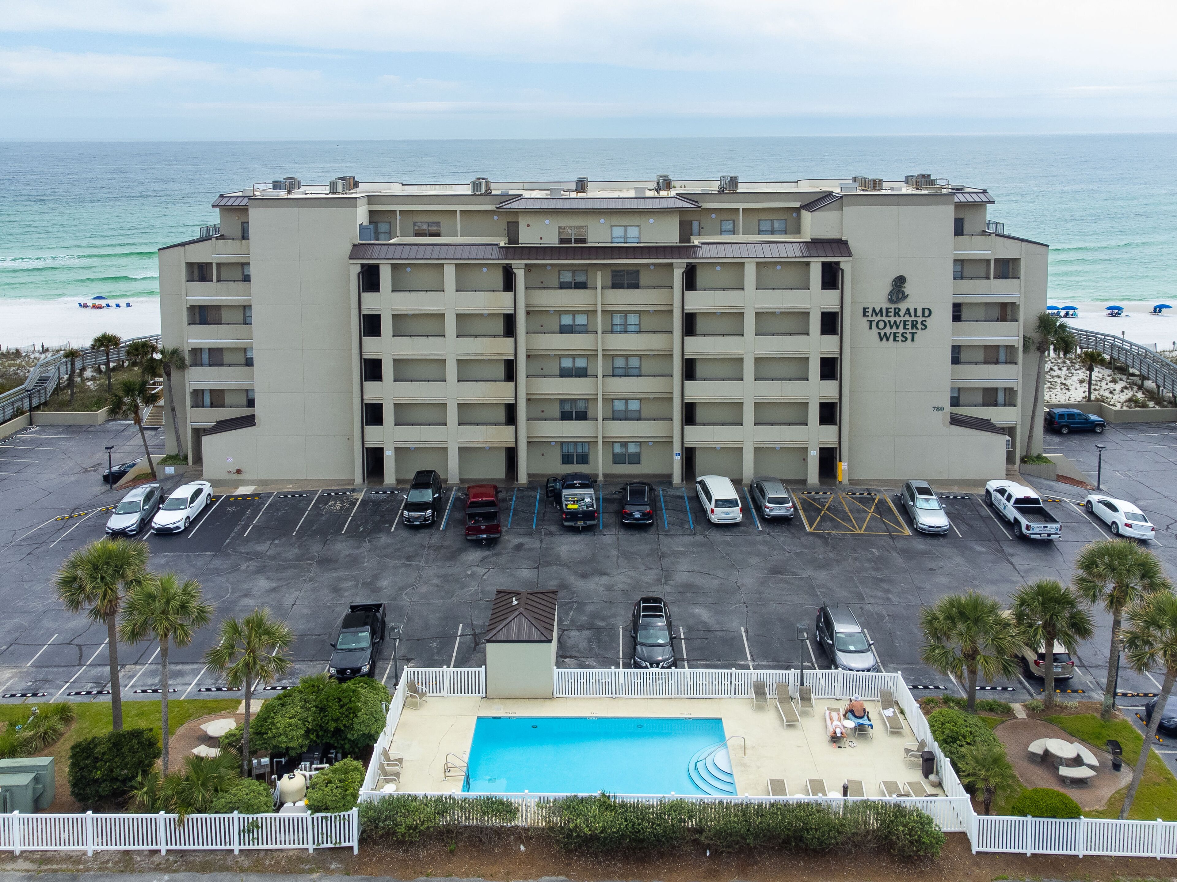 A multi-story hotel with a parking lot, a swimming pool, and a view of the beach.