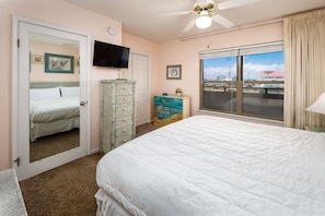 A bedroom with a bed, dresser, television, and a view of the city through the window.