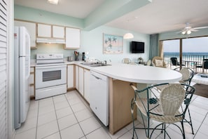 A kitchen with white appliances, a dining area with wicker chairs, and a view of the ocean.