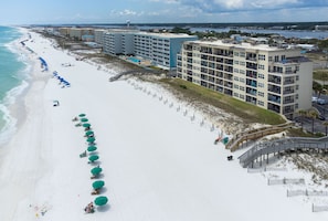 A beachfront hotel with multiple balconies, a pool, and a beach with umbrellas.