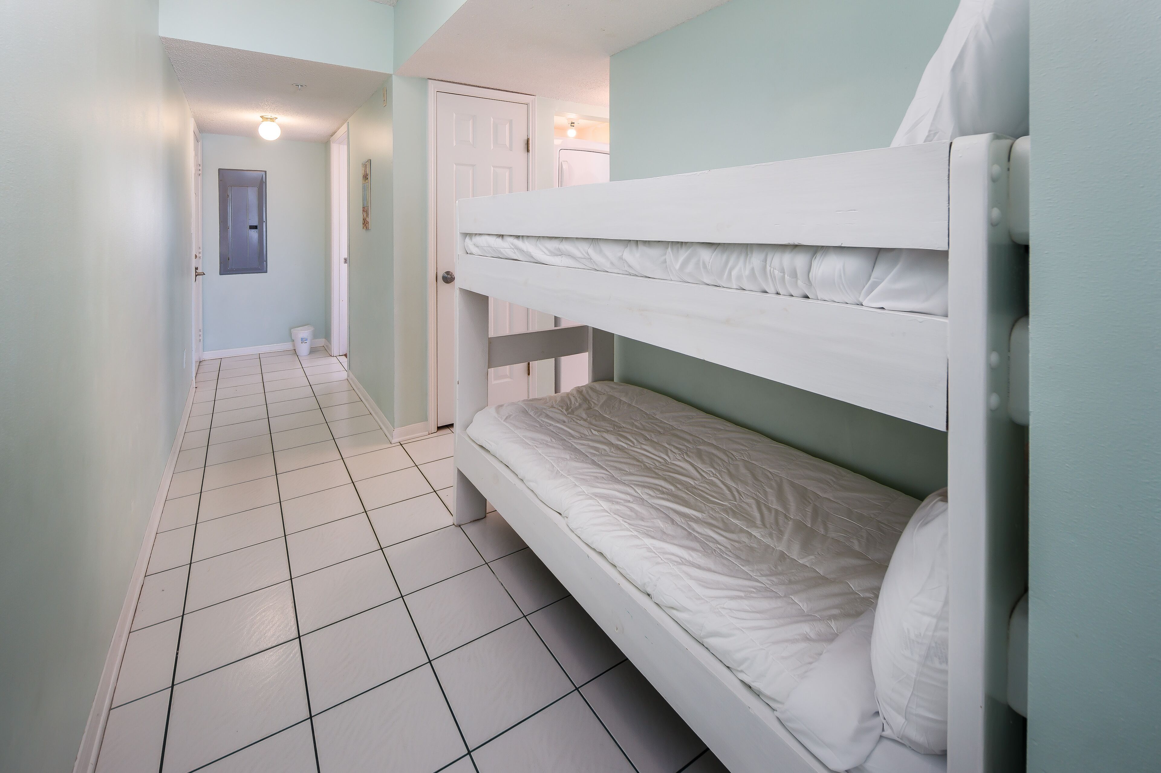 A room with a bunk bed, a door, a light fixture, and a tiled floor.