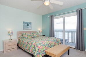 A bedroom with a bed, bedside tables, a ceiling fan, a window with curtains, and a view of the ocean. - First floor oceanfront condo in Ocean Dunes! (Kure Beach)