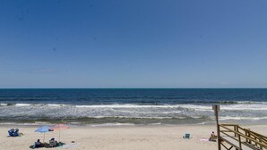 Une plage avec une promenade en bois, des gens se détendant sur le sable et un ciel bleu dégagé.