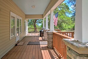 A covered porch with a wooden deck, a stone bench, an American flag, and a view of trees and sky. - Secluded & Quiet Atlantic Home: 1 Mi to Boat Ramp! (Atlantic)