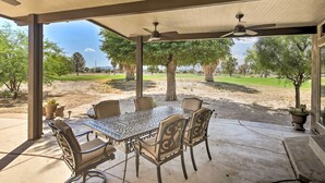 Un patio al aire libre con una mesa y sillas, un ventilador de techo y vistas a un campo de golf.