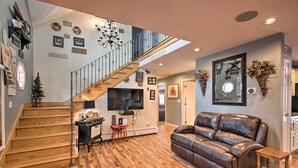 Un salon spacieux avec un canapé en cuir, un escalier en bois et un téléviseur à écran plat fixé au mur.