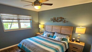A bedroom with a bed, wooden headboard, two bedside tables with lamps, a ceiling fan, and a window with blinds. - Condo # 102 Perfect 2 bedroom one bath condo directly across from  famous Siesta Key Beach. (Sarasota)