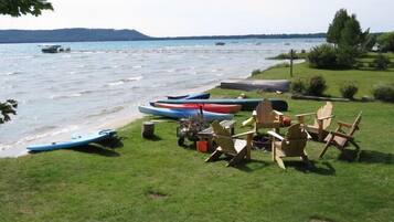 A lakeside setting with canoes, chairs, and a table on the grass near the water.