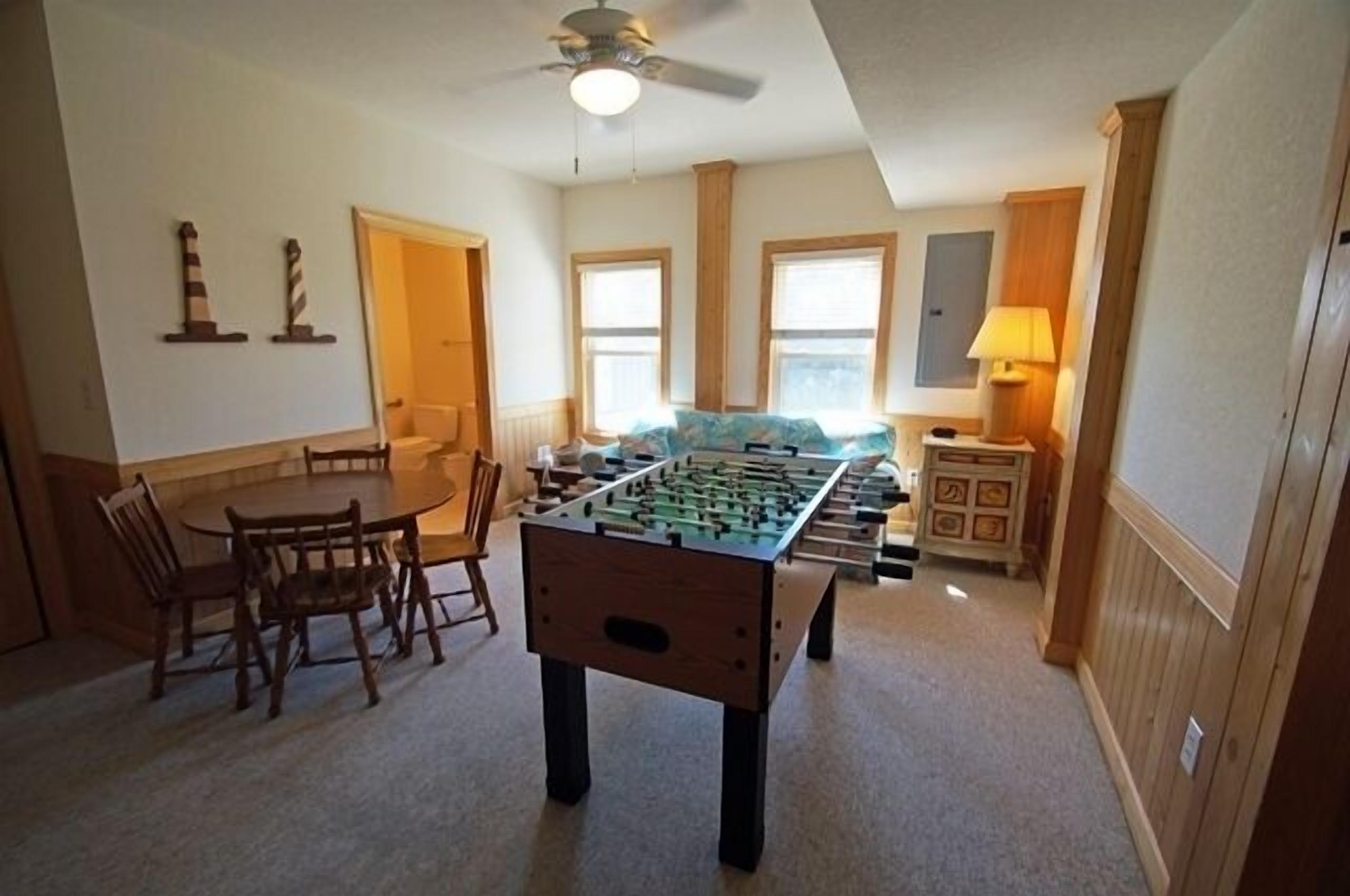 A cozy room with a foosball table, a dining table with chairs, and a ceiling fan.