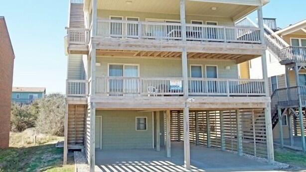 A two-story building with a balcony on the upper floor, a covered area on the ground floor, and a wooden deck. - KD904- Semi-OF favorite with elevator, 4 master suites and gourmet kitchen!! (Kill Devil Hills)