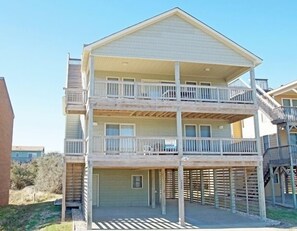A two-story building with a balcony on the upper floor, a covered area on the ground floor, and a wooden deck. - KD904- Semi-OF favorite with elevator, 4 master suites and gourmet kitchen!! (Kill Devil Hills)