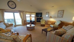 A living room with a sofa, armchairs, a coffee table, a fireplace, a television, and a large window with curtains. - KD904- Semi-OF favorite with elevator, 4 master suites and gourmet kitchen!! (Kill Devil Hills)