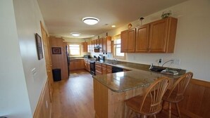A kitchen with wooden cabinets, a granite countertop, and a central island with bar stools. - KD904- Semi-OF favorite with elevator, 4 master suites and gourmet kitchen!! (Kill Devil Hills)
