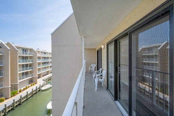 Un balcon avec des chaises blanches, une vue sur les immeubles voisins et un ciel dégagé.